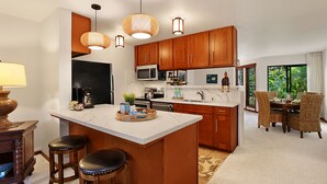 A modern kitchen with wooden cabinets, a marble countertop, and a central island with stools. - Waikomo Stream Villas 302 | Updated 1BR Condo w/ Cal King, AC, Murphy Bed (Koloa)