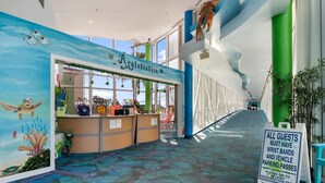 Un espace d’accueil intérieur agrémenté d’une fresque sur le thème de la mer, d’un comptoir de réception et d’un panneau indiquant aux visiteurs de se rendre au comptoir d’enregistrement pour obtenir leurs bracelets et leurs laissez-passer pour les véhicules.