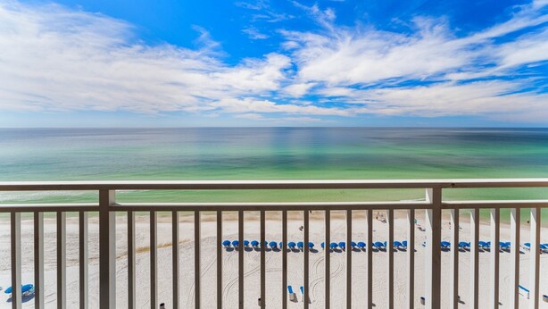 Une vue sur la plage depuis un balcon doté d’une balustrade, avec un ciel dégagé et l’océan à l’horizon.