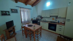 Een kleine keuken met een eettafel, stoelen, een televisie en essentiële apparaten.