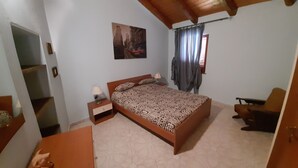 Een slaapkamer met een bed, nachtkastje, lamp, stoel en een schilderij aan de muur.