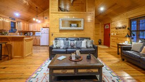 L’intérieur d’une cabane comprend un plafond en bois, un coin cuisine, un salon avec un canapé et un espace repas.