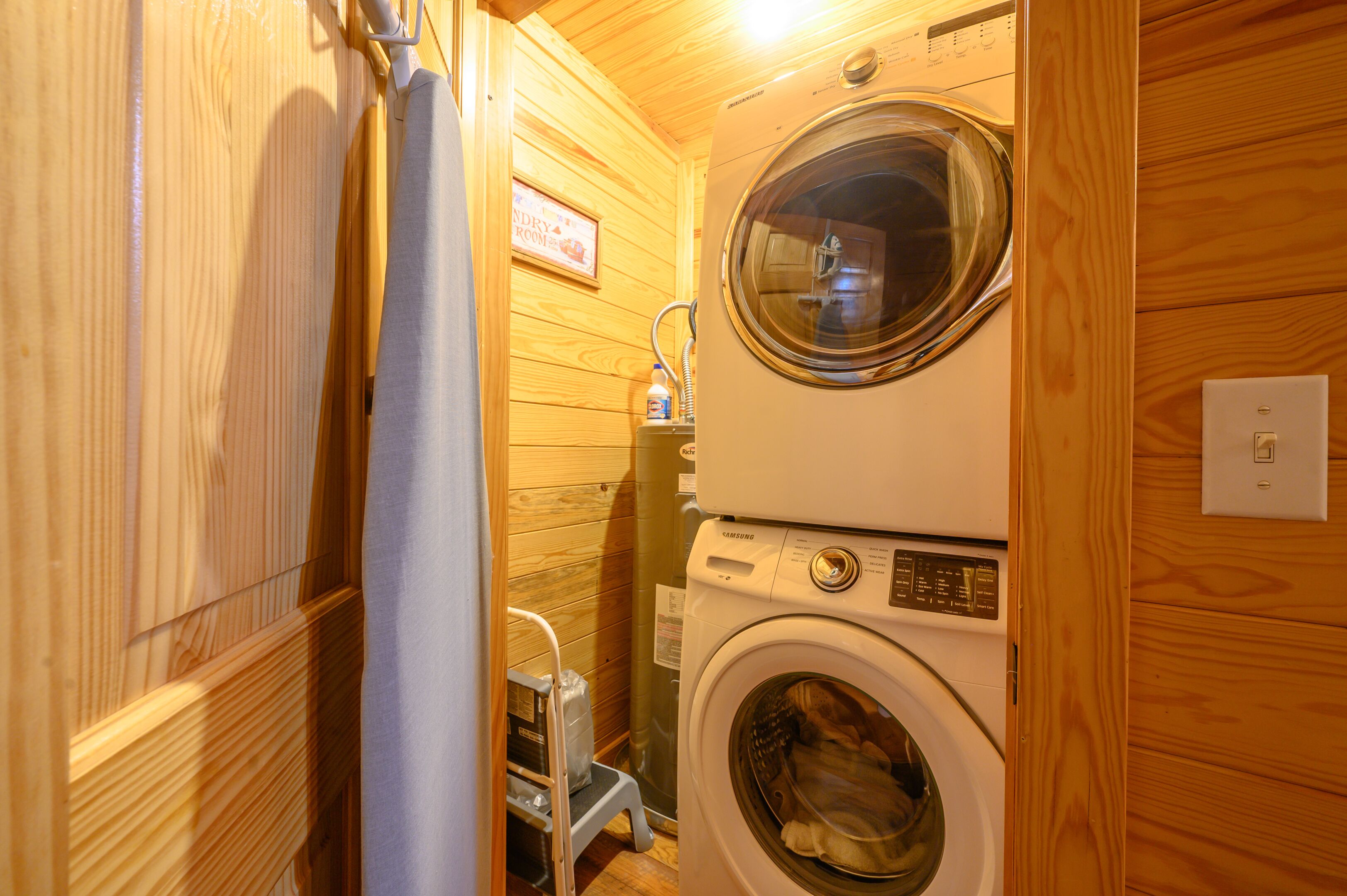 Une petite buanderie équipée d’un lave-linge et d’un sèche-linge à chargement frontal, avec des murs en bois et un petit tabouret.