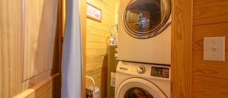 Une petite buanderie équipée d’un lave-linge et d’un sèche-linge à chargement frontal, avec des murs en bois et un petit tabouret.