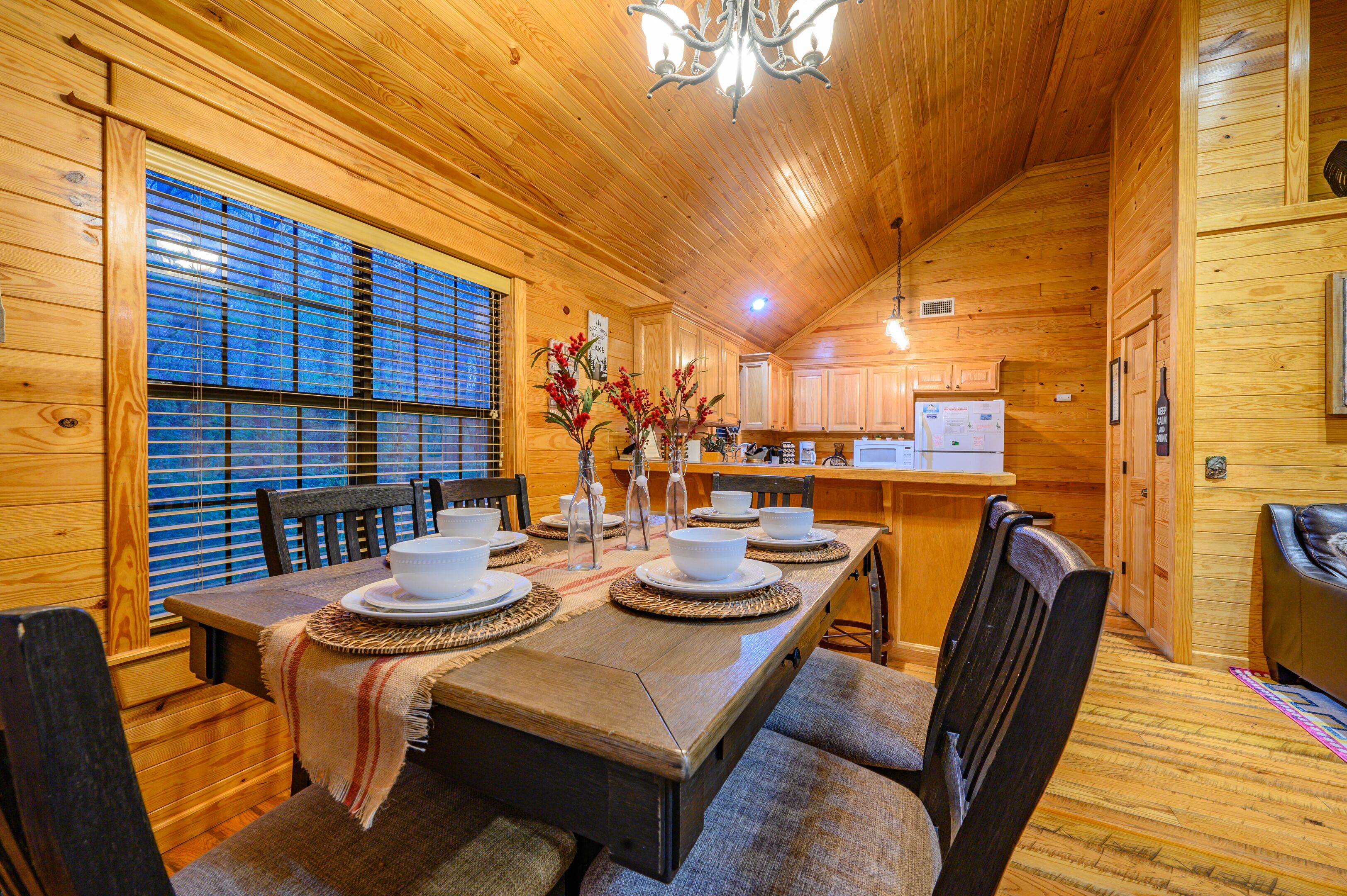 A wooden interior with a dining table set for four, a kitchen area, and a cozy seating area with a fireplace.