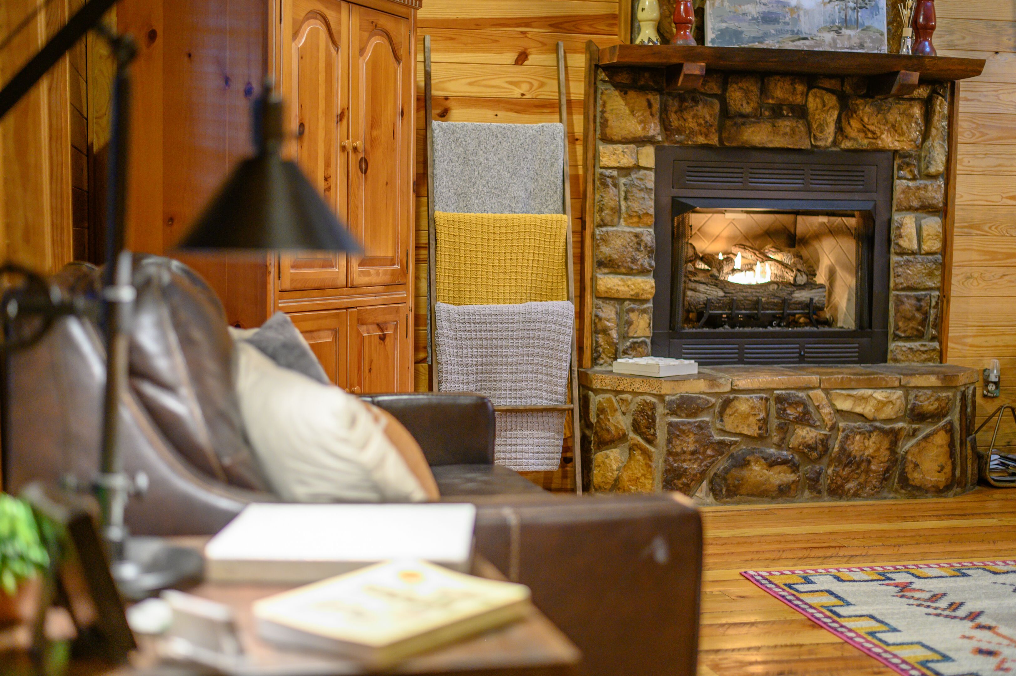 A cozy living room with a stone fireplace, wooden walls, and a leather sofa.