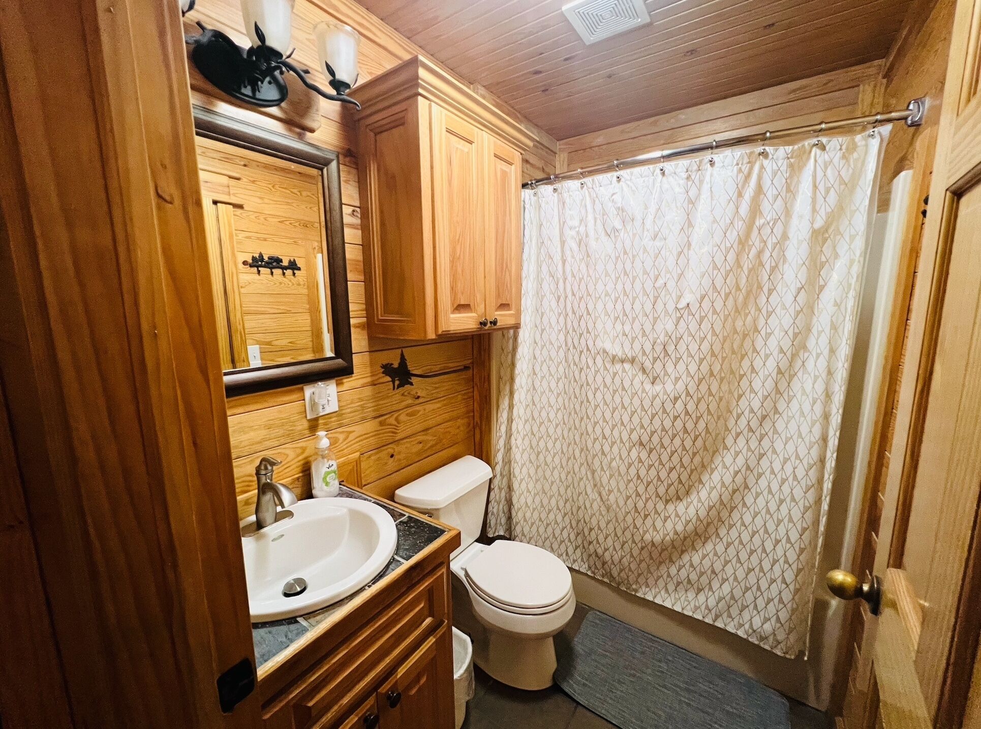 A wooden-paneled bathroom with a sink, mirror, toilet, and shower curtain.
