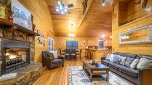Un intérieur chaleureux de chalet en bois, avec une cheminée, des canapés en cuir, un coin repas et une cuisine.