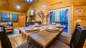 L’intérieur d’un chalet en bois, avec une table à manger dressée pour quatre personnes, un canapé et une vue sur l’extérieur par une porte.