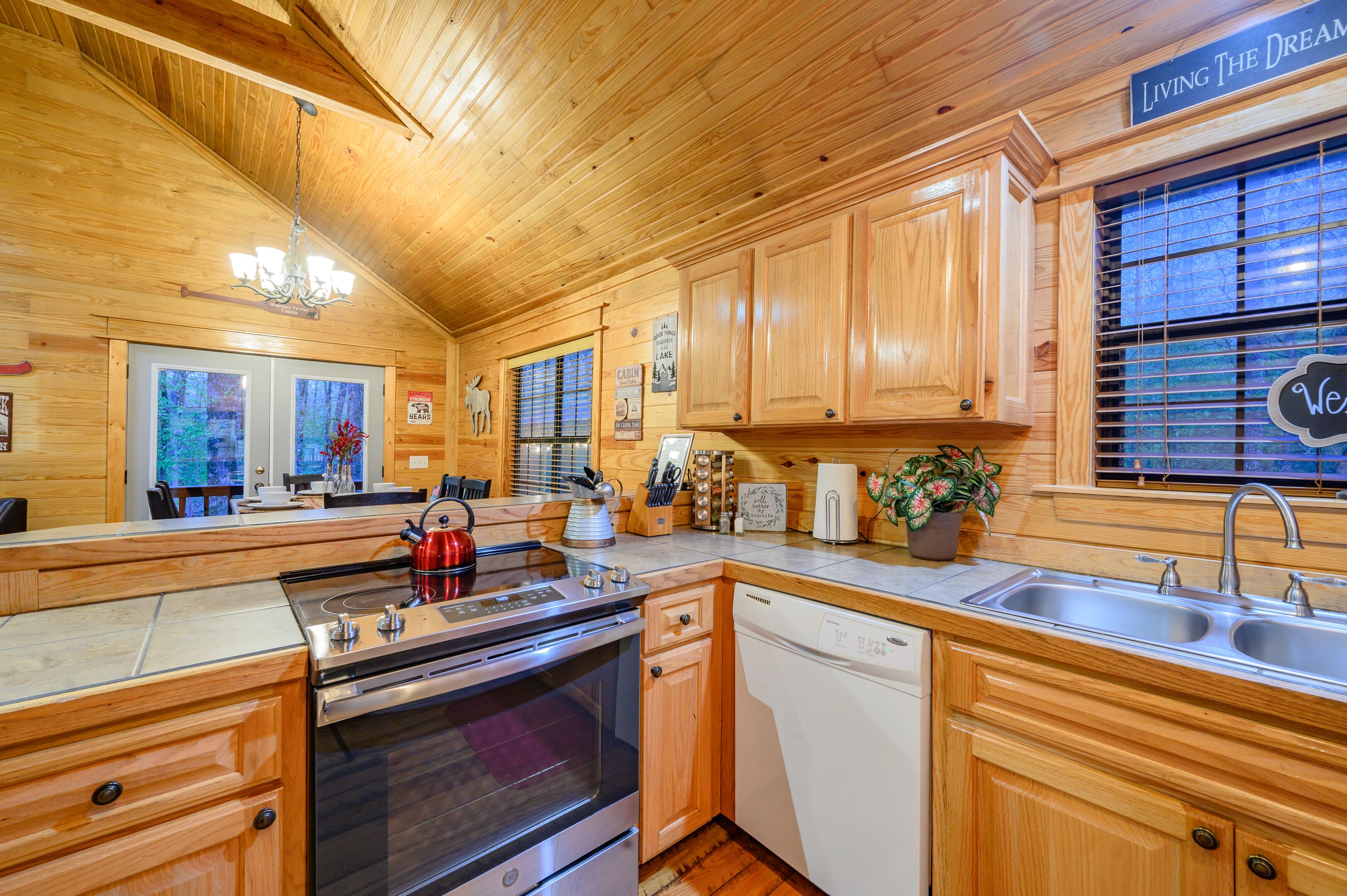 A wooden cabin-style kitchen with a stove, oven, dishwasher, and a large window with blinds.