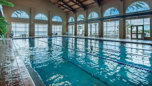 Une piscine intérieure à l’eau claire, entourée de grandes baies vitrées qui offrent une vue sur les palmiers et la mer.
