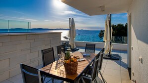 A balcony with a table set for dining, overlooking a body of water with a clear sky. - Crystal Holiday Residence (Sukosan)