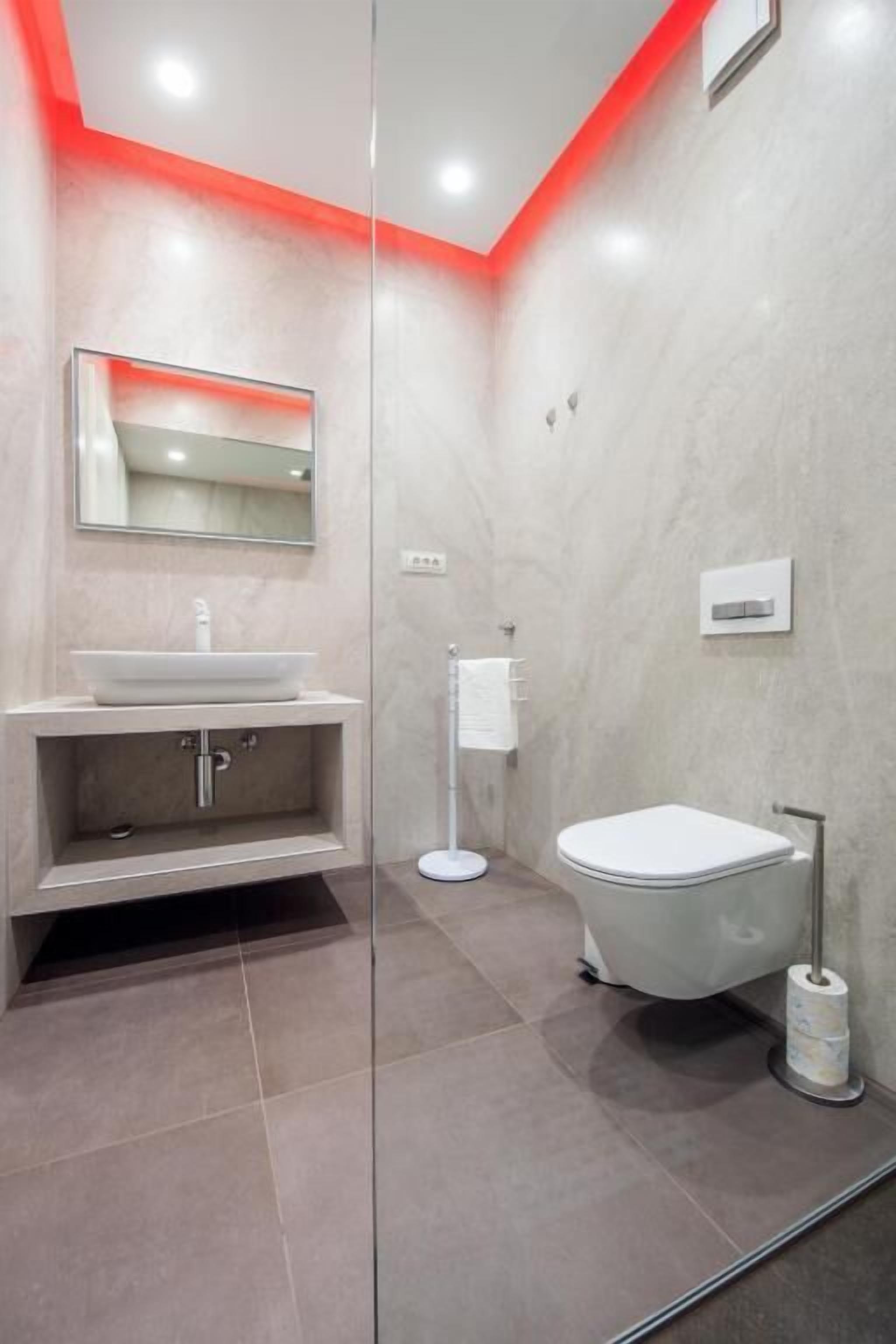 Ein modernes Badezimmer mit Glasabtrennung, Waschbecken mit Spiegel, Toilette und Handtuchhalter.