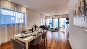 A modern dining area with a long table set for four, a sofa, and a view of the outdoors. - Crystal Holiday Residence (Sukosan)