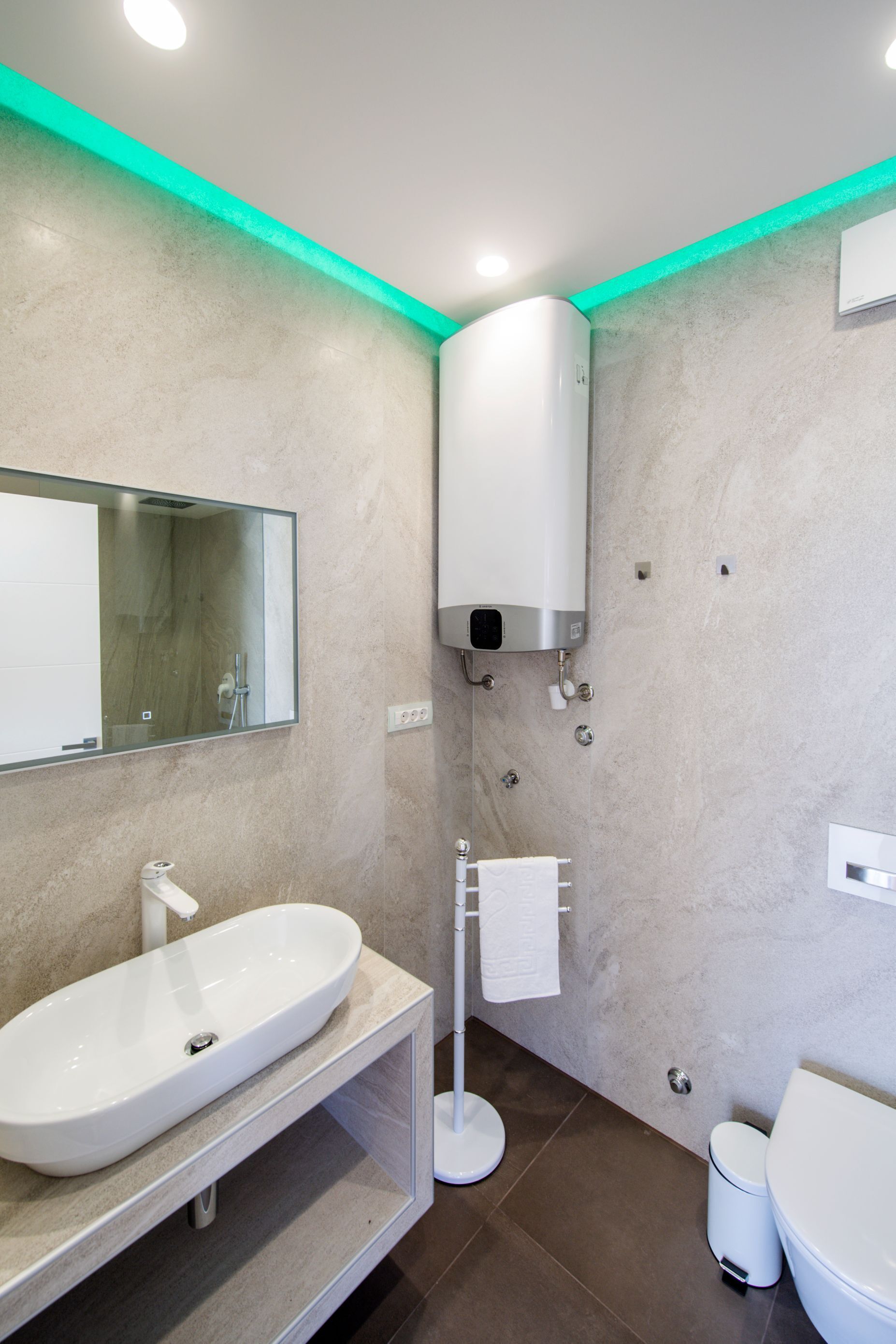 A modern bathroom with a large mirror, a white sink, a toilet, and a wall-mounted heater.
