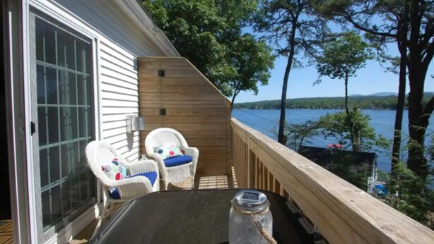 Eine Terrasse mit zwei Korbstühlen, einem Tisch und Blick auf einen See.