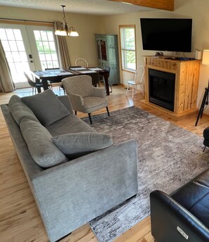 A living room with a grey sofa, a fireplace, a flat-screen TV, and a dining area with a table and chairs.