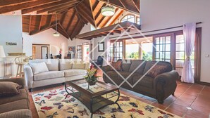 A spacious living room with a high ceiling, wooden beams, and large windows. There are two sofas, a coffee table, and a patterned rug. - Beautiful 5 bed-rooms Villa at Terres Basses (Saint Martin)