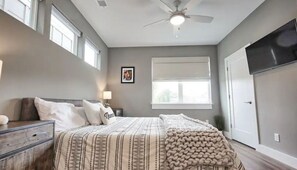 Ein Schlafzimmer mit Bett, Nachttischen, Deckenventilator, Fenster und Tür.