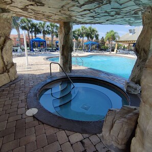 A hot tub area with a pool, stone pillars, and lounge chairs. - Moderno Townhouse 4 hab· Piscina · Resort con Cine & Tobogán, 8 millas de Disney (Kissimmee)