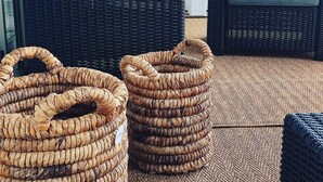 Ett rum med möbler av rotting, inklusive en soffa och två fåtöljer, och två stora, flätade korgar på golvet.