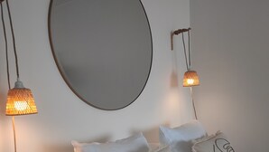 Ett sovrum med en stor, rund spegel, två sänglampor och tre kuddar med ansiktsmotiv.