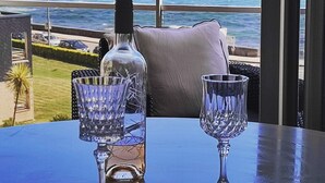 Ett bord med två kristallglas och en flaska, med utsikt över en strand och havet.