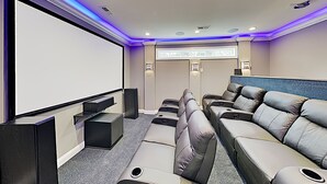 Ein Heimkino mit großer Leinwand, mehreren Sitzbereichen und Teppichboden.