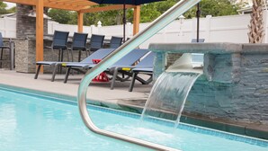 Ein Pool mit Wasserfall, Liegestühlen und einer überdachten Sitzgruppe.