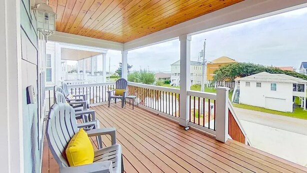 Eine überdachte Veranda mit Holzboden und weißen Geländern, ausgestattet mit Gartenmöbeln und Kissen.