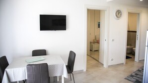 A dining area with a table and chairs, a flat-screen TV mounted on the wall, and a clock on the wall. - Nice apartment not far from the sea (Lacco Ameno)