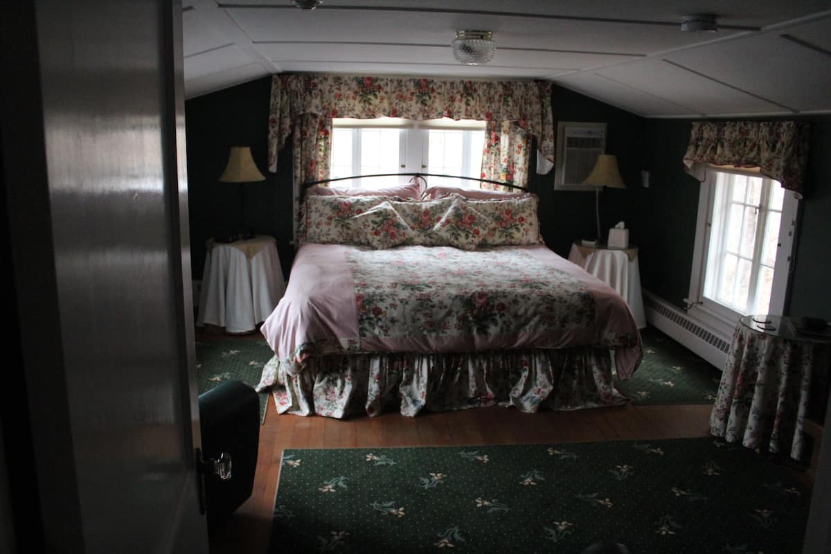 A bedroom with a large bed, floral curtains, and a green carpet.