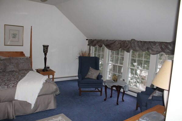 A bedroom with a bed, two chairs, a table, and a window with curtains. - Fox Creek Inn LLC (Chittenden)