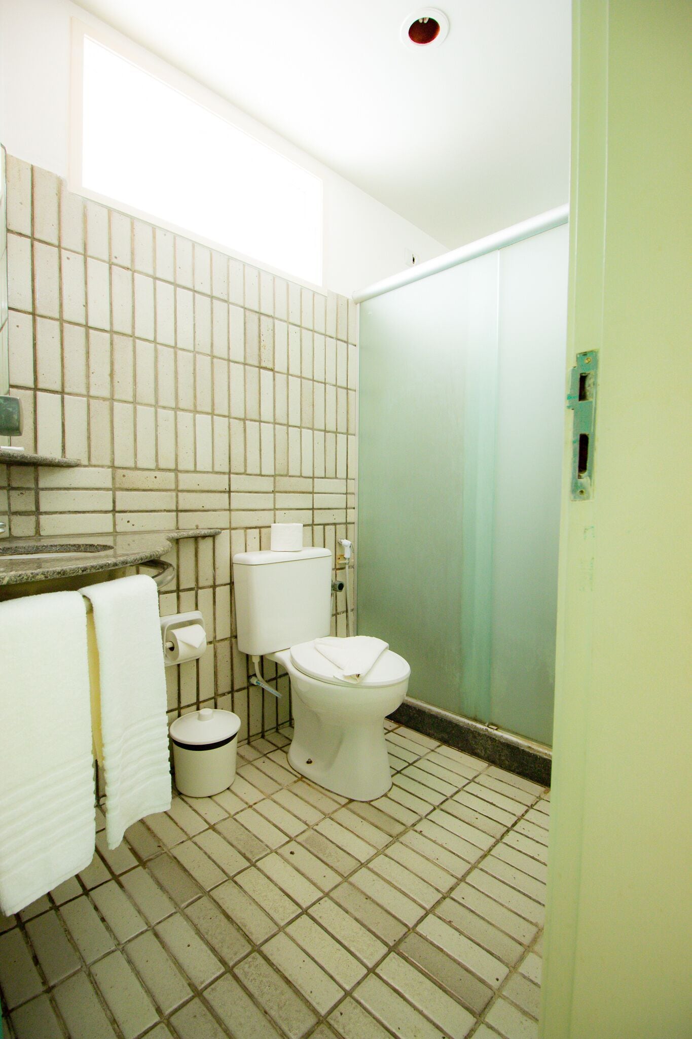 Een kleine betegelde badkamer met toilet, wastafel en een prullenbak.