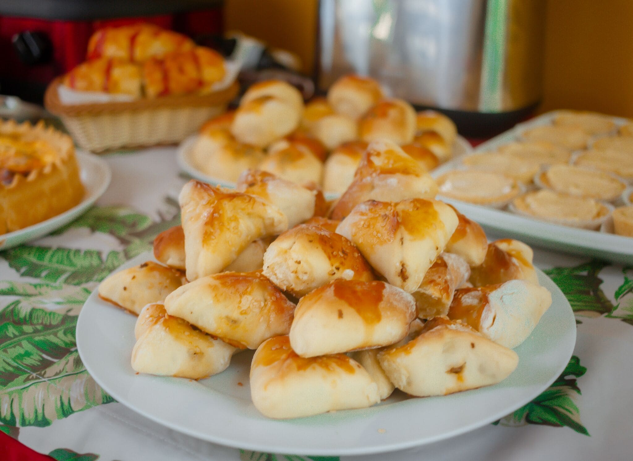 A table with various baked goods, including bread rolls and pastries, on a patterned tablecloth.