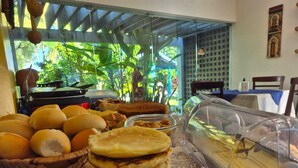 A breakfast buffet with bread, pastries, and a glass display case. - Pousadar Marahú (Ipojuca)