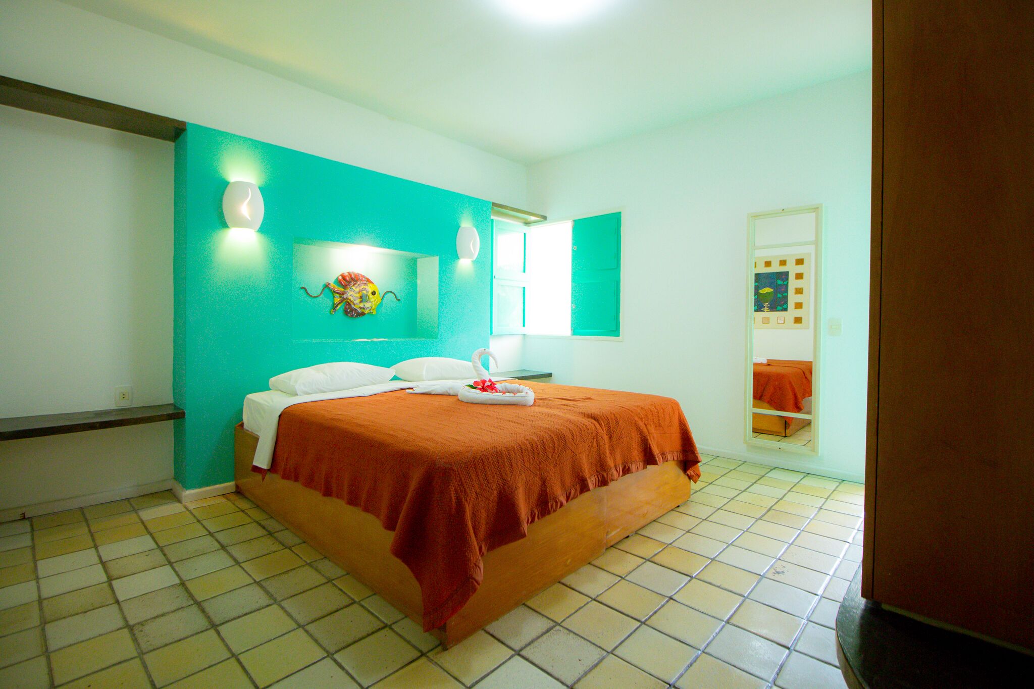 A hotel room with a bed, a mirror, and a wall-mounted light fixture.