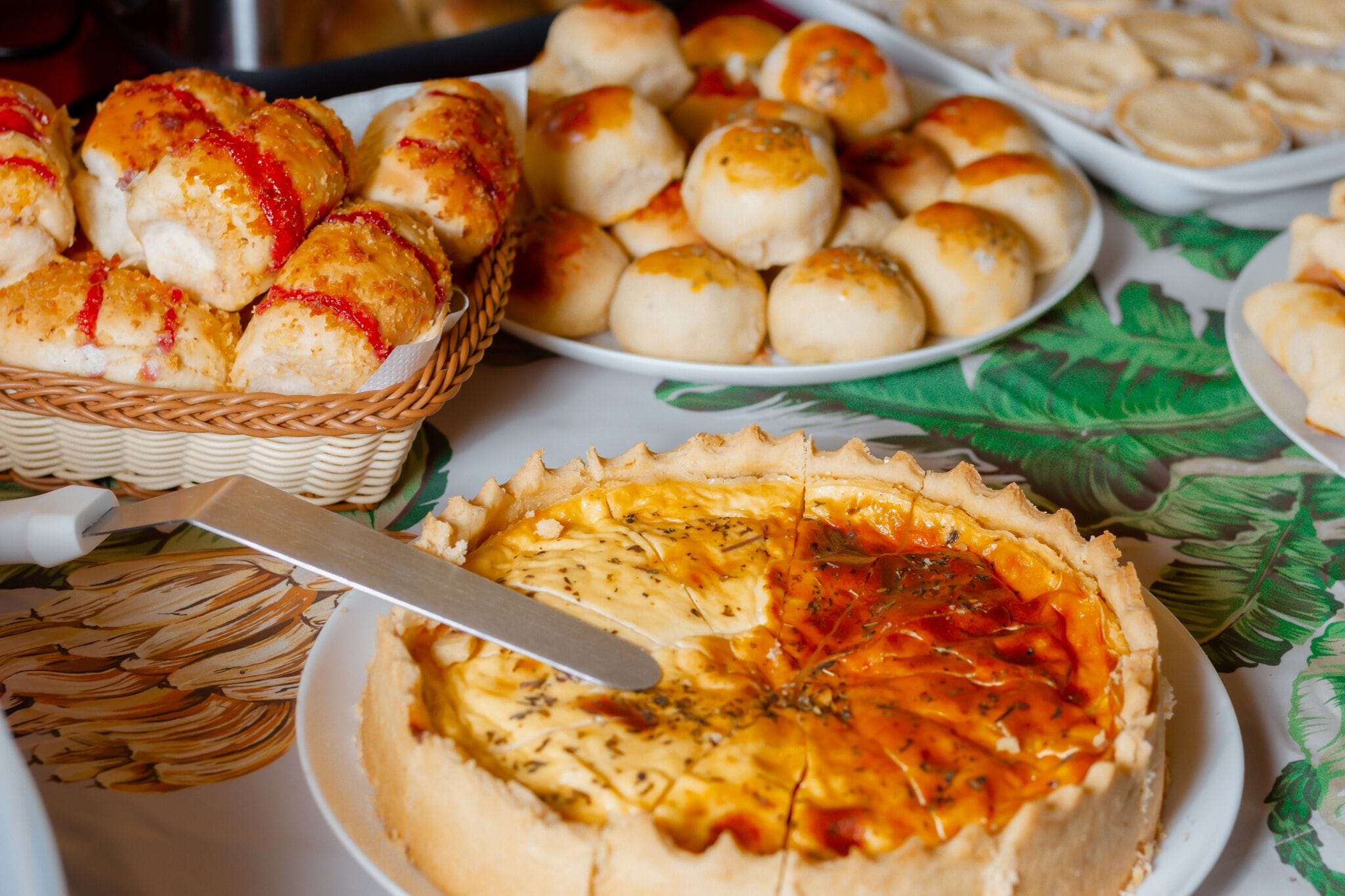Una mesa con diversas opciones de panadería, incluyendo una tarta, panecillos y pan.