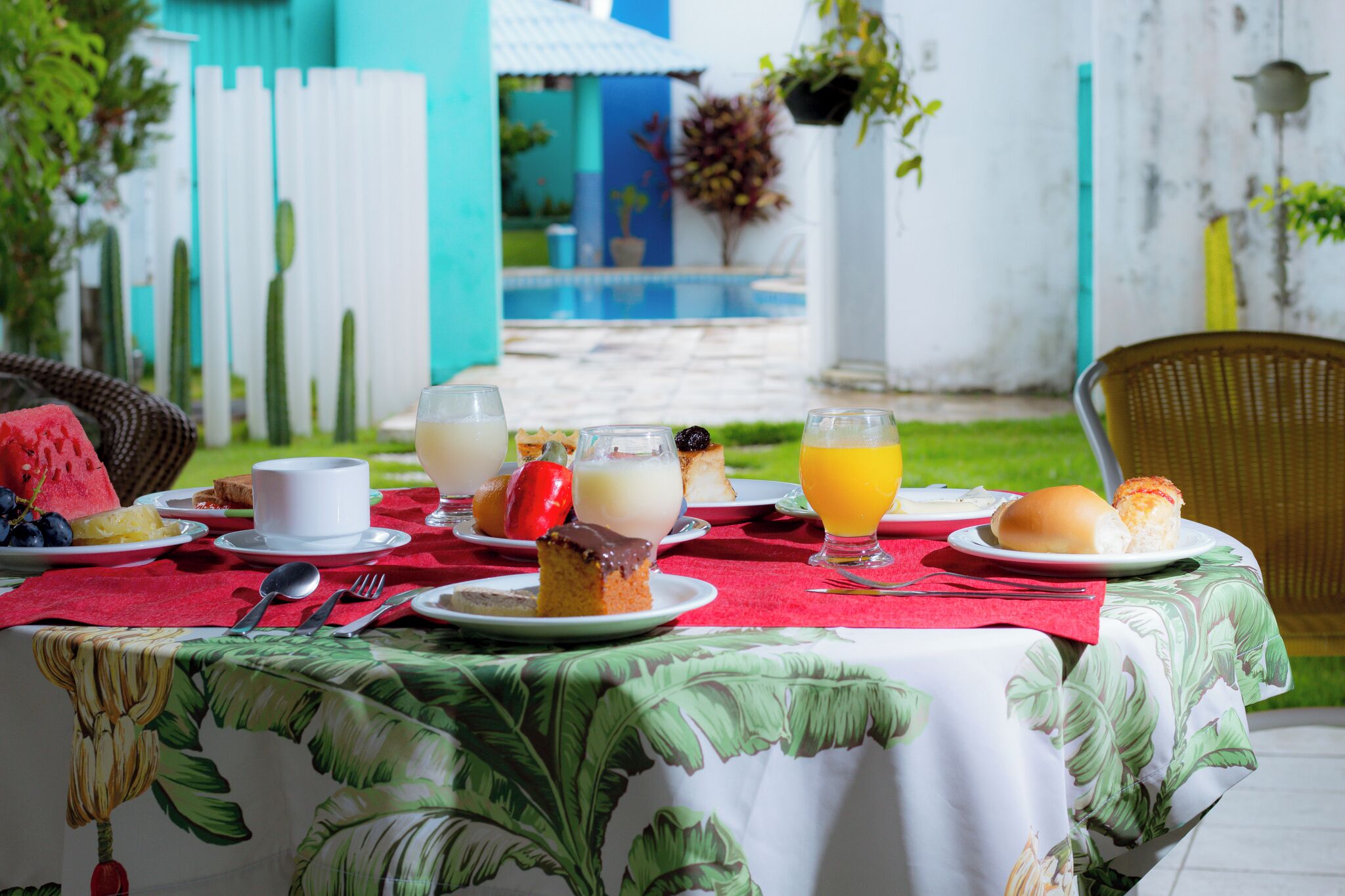 Una mesa puesta al aire libre con mantel rojo, platos de comida y bebidas.