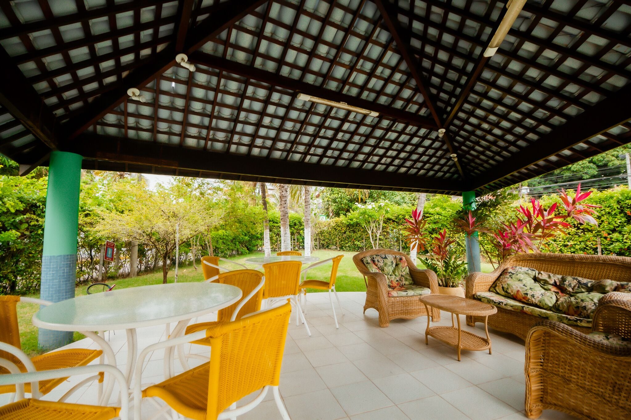 An outdoor patio with a covered area, furnished with wicker chairs and tables, surrounded by lush greenery.