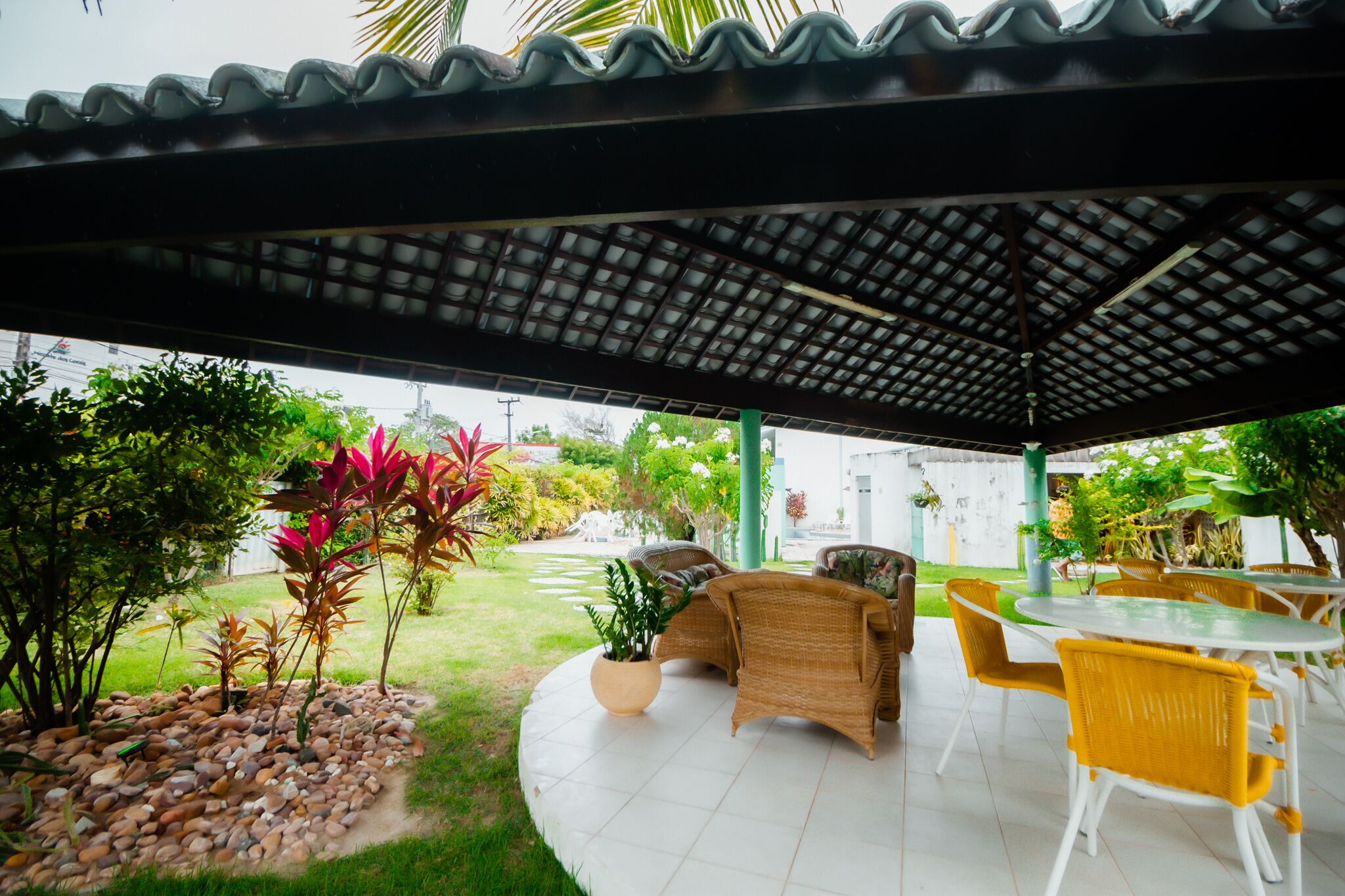 An outdoor patio area with wicker furniture, a covered section, and a garden with various plants.