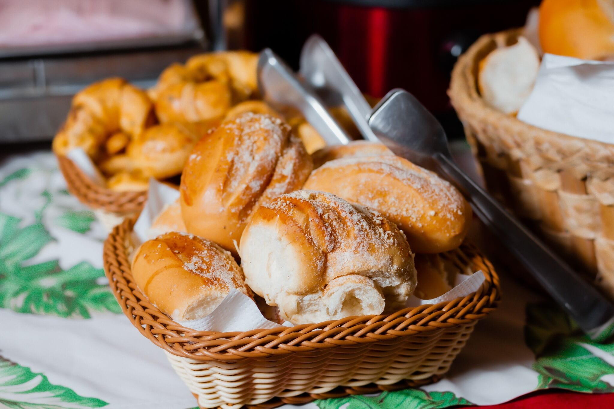 Un panier rempli de viennoiseries est posé sur une table recouverte d’une nappe à motifs verts.