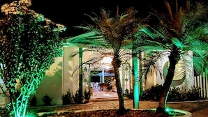 A nighttime view of a hotel with a well-lit entrance, palm trees, and a pathway leading to the building. - Pousadar Marahú (Ipojuca)