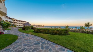 A stone pathway leading to a pool area with a view of the ocean and a resort building. - TheNest. Oceanview condo with access to infinity pool and jacuzzi (San José del Cabo)