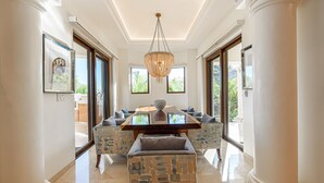 A spacious dining area with a central table, surrounded by patterned chairs and a bench, under a hanging chandelier. - TheNest. Oceanview condo with access to infinity pool and jacuzzi (San José del Cabo)