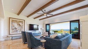A spacious living room with a large sofa, two armchairs, a coffee table, and a flat-screen TV. The room features a high ceiling with exposed wooden beams and a large window offering a view of the ocean. - TheNest. Oceanview condo with access to infinity pool and jacuzzi (San José del Cabo)