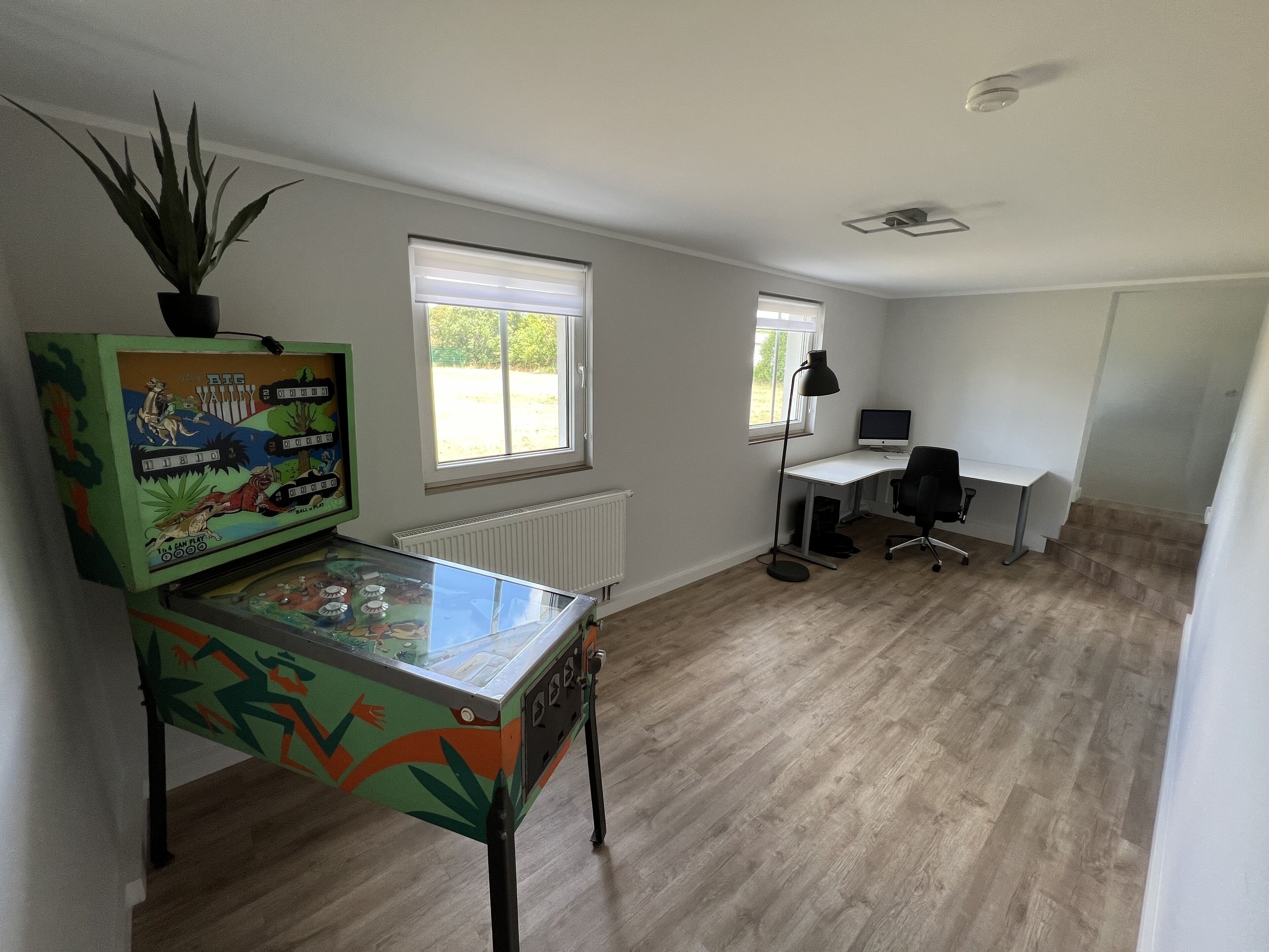 Una habitación con escritorio, computadora y una máquina de pinball colorida.