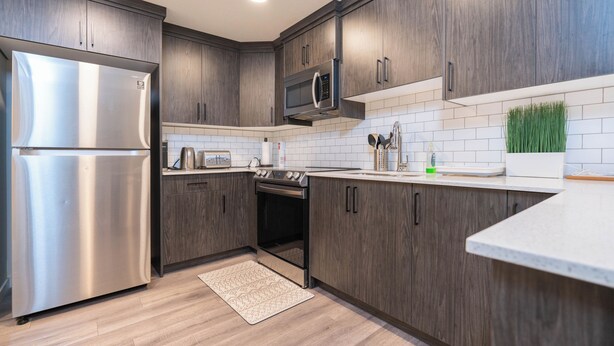 Une cuisine moderne avec des meubles en bois foncé, des appareils électroménagers en acier inoxydable et un dosseret de carrelage blanc.