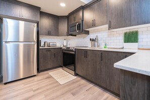 A modern kitchen with dark wood cabinets, stainless steel appliances, and a white tiled backsplash. - When you want a little more than a couch. (Calgary)