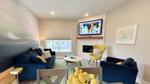 A modern living room with a sofa, armchairs, a coffee table, and a TV mounted on the wall. - New 3 bed 4 bath home - rooftop deck, 2 car garage & porch near downtown! (Omaha)